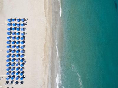 Letecký pohled na pláž s modrými slunečníky a tyrkysovou vodou.