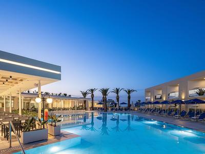 Modern hotel pool area at sunset with seating and palm trees.