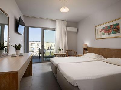 Modern hotel room with two single beds, desk, TV, and city view.