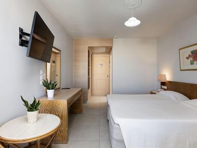 Modern hotel room with double bed, wall TV, and seating area with plants.