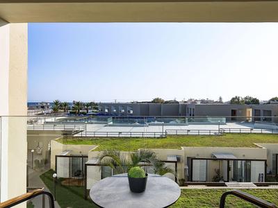 View from a balcony overlooking a hotel pool and garden under clear skies.