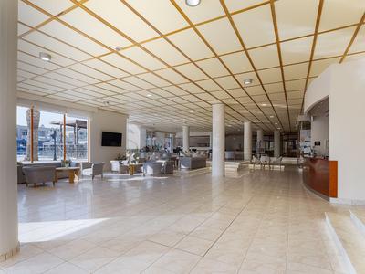 Spacious hotel lobby with light tiled floors, columns, and seating areas under a patterned ceiling.