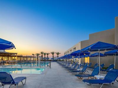 Modern pool area with blue lounge chairs and umbrellas at sunset.