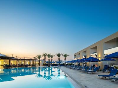 Modern hotel pool with blue umbrellas and palm trees at sunset.