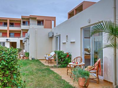 Vor der Hotelanlage befinden sich kleine Terrassen mit Tischen, Stühlen und Pflanzen.