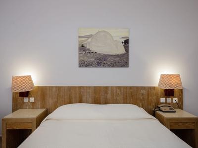 Ein schlichtes Schlafzimmer mit weißer Wand, Holzkopfteil, zwei Nachttischen und Lampe auf jeder Seite.