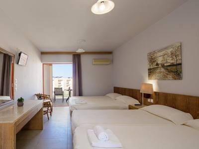 Helles Hotelzimmer mit zwei Doppelbetten, Holzmöbeln, Balkon und Meerblick.