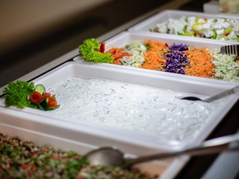 Bufet s několika čerstvými a barevnými pokrmy, včetně bílého dresinku a nastrouhané zeleniny.