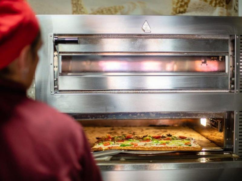 Profesionální trouba peče velkou pizzu, šéfkuchař ji pozorně sleduje.