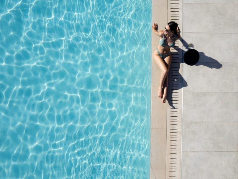 Žena v plavkách leží vedle bazénu s čistou modrou vodou.