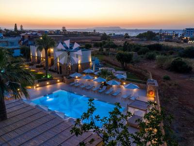 Widok na oświetlony hotelowy basen z palmami i leżakami wieczorem.