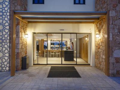 Oświetlone wejście do hotelu z przeszklonymi drzwiami i kamiennymi ścianami o zmierzchu