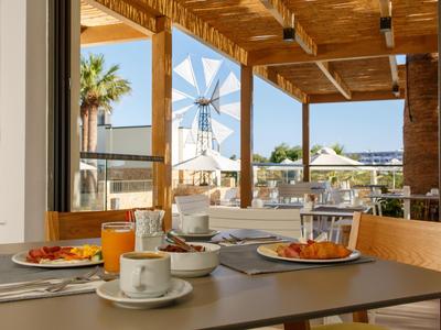 Stół śniadaniowy z kawą, sokiem i rogalikami na słonecznym tarasie z widokiem na wiatrak.