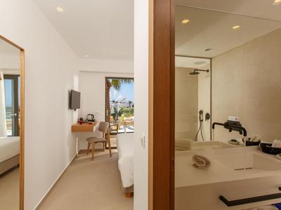 Nowoczesny pokój hotelowy z łóżkiem, biurkiem, lustrem oraz łazienką z umywalką i prysznicem.