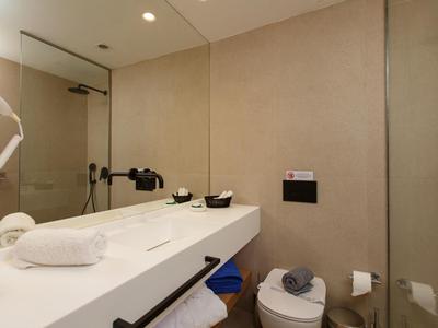 Nowoczesna łazienka z białym blatem, lustrem, toaletą i neutralnymi ścianami.