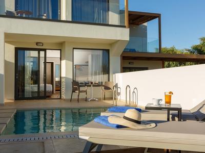 Nowoczesny basen z leżakami, stołem i osłoną przeciwsłoneczną przed pokojem hotelowym ze szklaną balustradą.