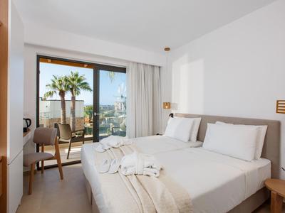 Jasno urządzone pokoje hotelowe z dwoma łóżkami i balkonem z widokiem na miasto.