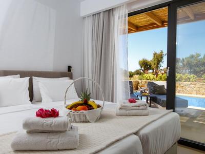 Accogliente letto matrimoniale con asciugamani bianchi e cesta di frutta vicino a una terrazza con vista piscina.