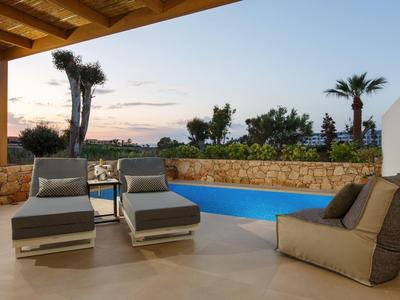 Taras z basenem, wygodne leżaki i widok na palmy o zachodzie słońca.