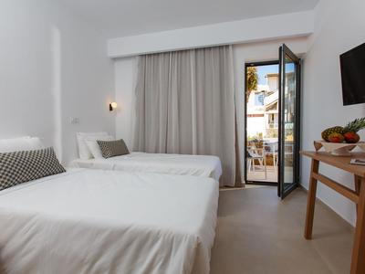 Helles Hotelzimmer mit zwei Einzelbetten, TV, Schreibtisch und Blick auf einen Balkon.