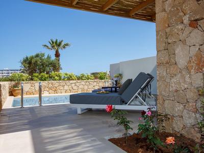 Terrazza con lettini prendisole con vista su piscina e palme con tempo soleggiato.
