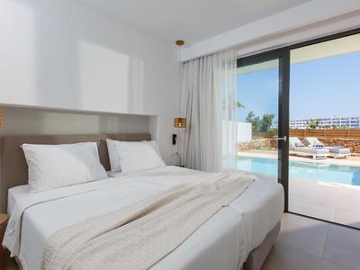 Helles Schlafzimmer mit Doppelbett und Blick auf Pool und Gebäude durch große Glasschiebetür.