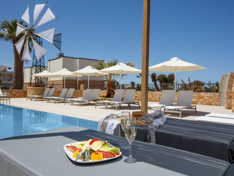 Nowoczesny basen z leżakami, parasolami i wiatrakiem pod jasnym niebem.