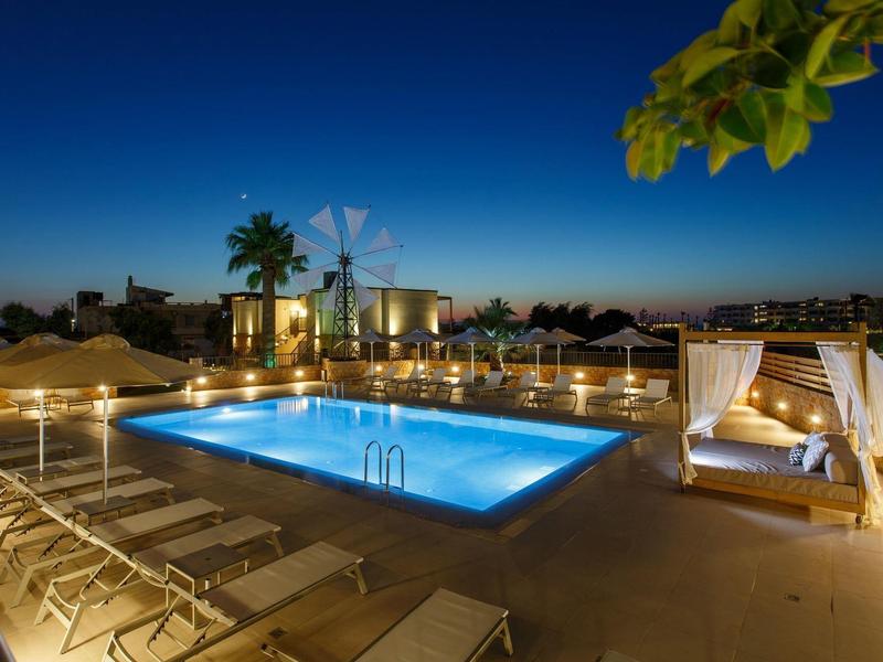 Oświetlony basen z leżakami i przytulną cabaną o zmierzchu.