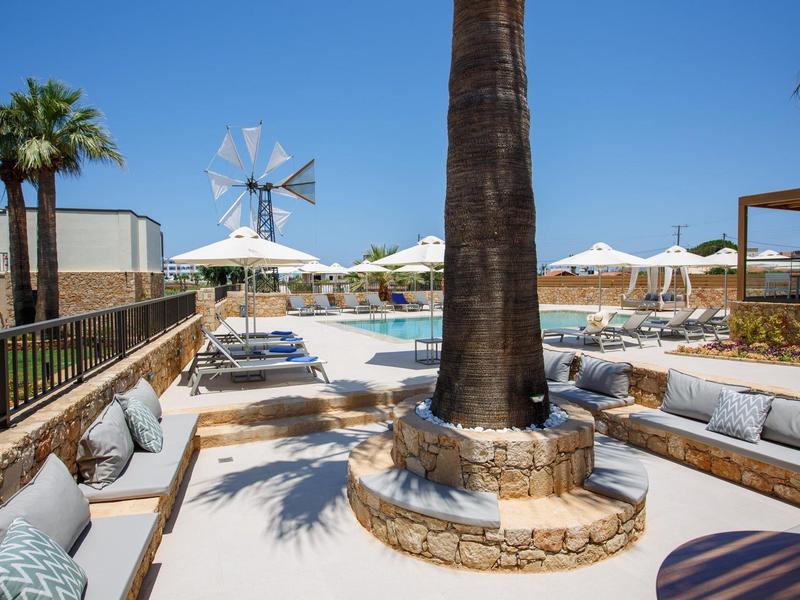 Słoneczny basen z leżakami, palmami i wiatrakiem pod czystym niebieskim niebem.