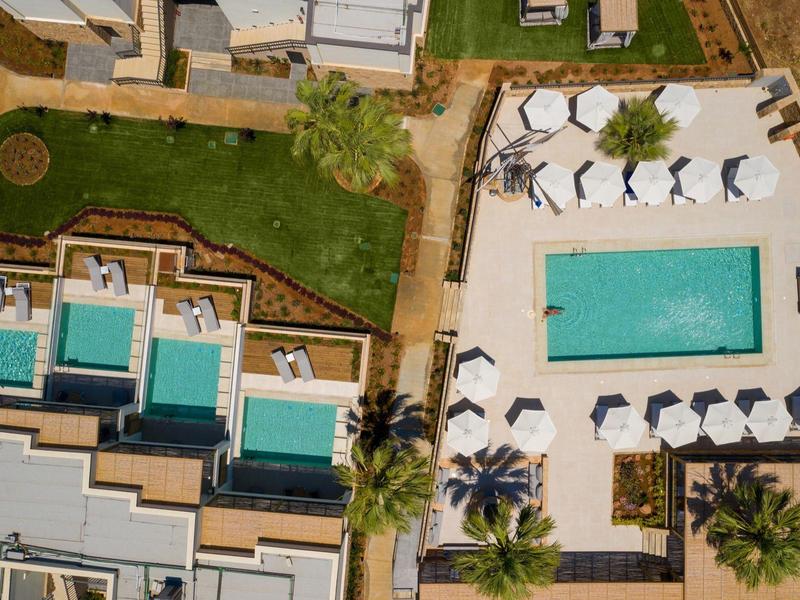 Widok z lotu ptaka na basen hotelowy z leżakami i sąsiednimi pokojami z prywatnymi basenami.