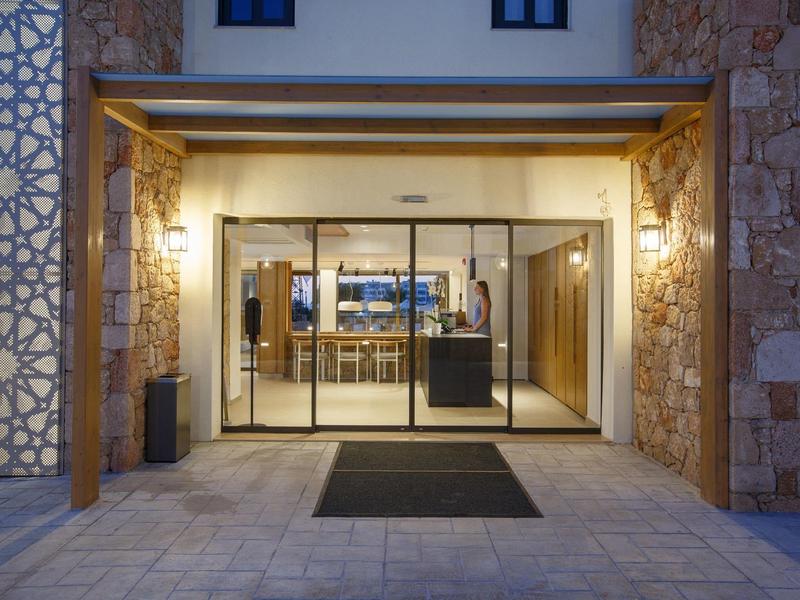 Oświetlone wejście do hotelu z przeszklonymi drzwiami i kamiennymi ścianami o zmierzchu