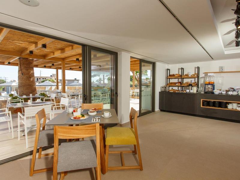 Jasna restauracja hotelowa z drewnianymi meblami, dużymi oknami i widokiem na taras.