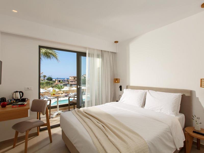 Jasny pokój hotelowy z łóżkiem podwójnym, małym biurkiem i widokiem na basen i morze.