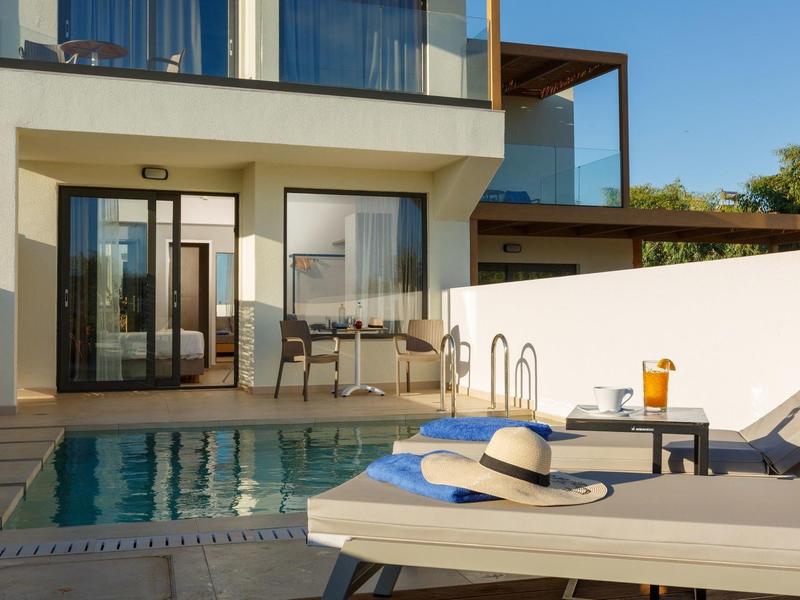 Nowoczesny basen z leżakami, stołem i osłoną przeciwsłoneczną przed pokojem hotelowym ze szklaną balustradą.