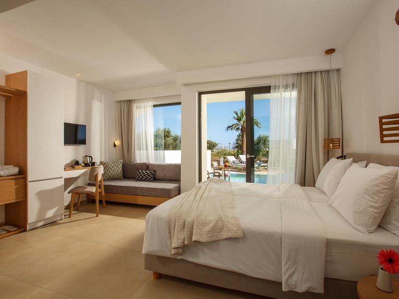 Jasny pokój hotelowy z dużym łóżkiem, sofą i widokiem na basen i palmy