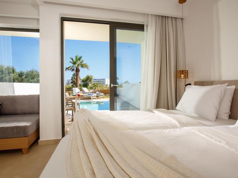 Jasny pokój hotelowy z łóżkiem podwójnym i balkonem z widokiem na basen i palmy.