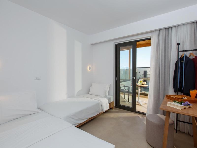 Jasny pokój hotelowy z dwoma łóżkami, balkonem i widokiem na miasto.