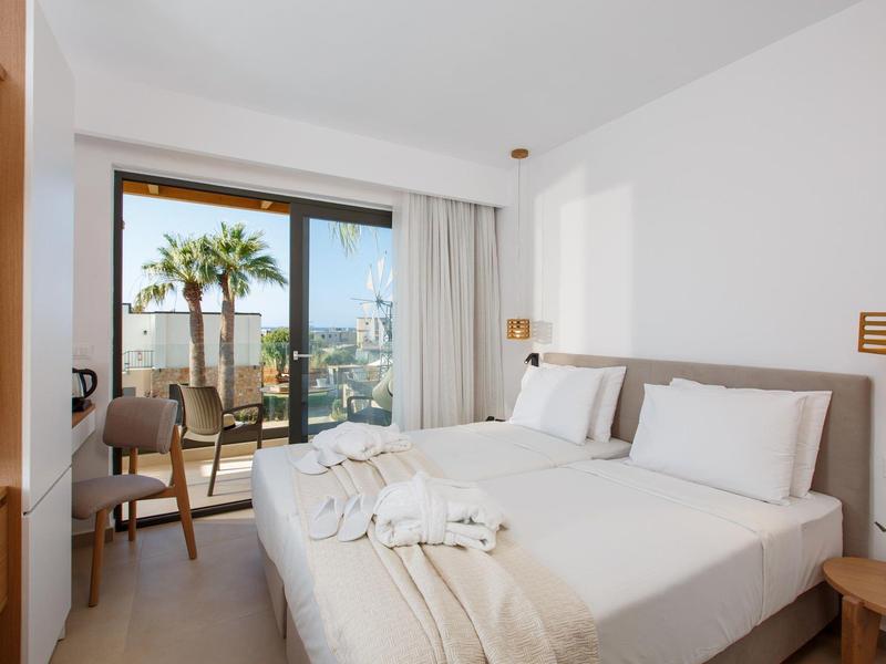 Jasno urządzone pokoje hotelowe z dwoma łóżkami i balkonem z widokiem na miasto.