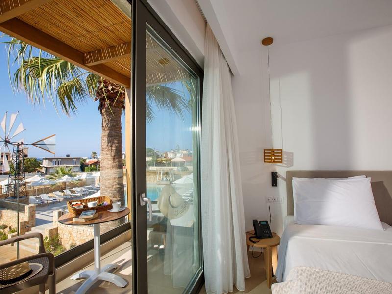 Widok z pokoju hotelowego z balkonem na słoneczny taras i palmy.