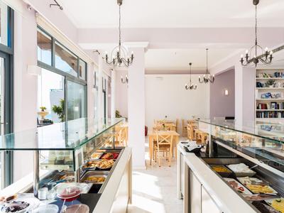 Licht café met glazen vitrines vol gebak en houten stoelen in eetgedeelte.