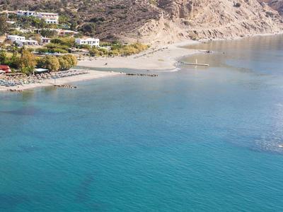 Koel strand met helder blauw water en bergen op de achtergrond.