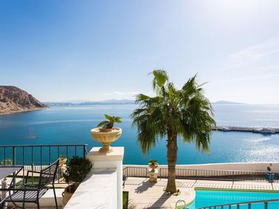 Schöne Aussicht auf das Meer und einen Pool von einer Terrasse mit Stühlen und einem Palmenbaum.