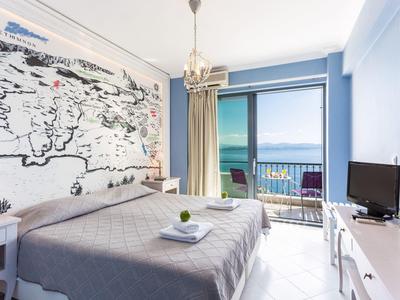 Lichte hotelkamer met tweepersoonsbed en uitzicht op zee door glasramen.