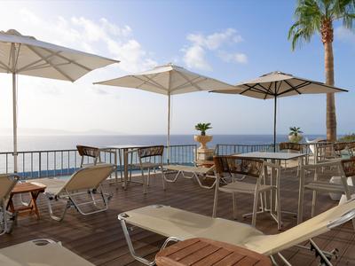 Terrasse mit Liegestühlen, Tischen und Sonnenschirmen mit Meerblick an einem sonnigen Tag