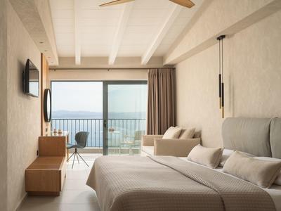 Helles Hotelzimmer mit Bett, Sofa, Balkon und Meerblick.