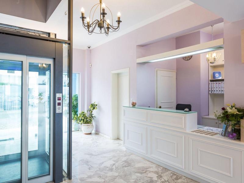 Lichte hotellobby met lift en witte receptiebalie.