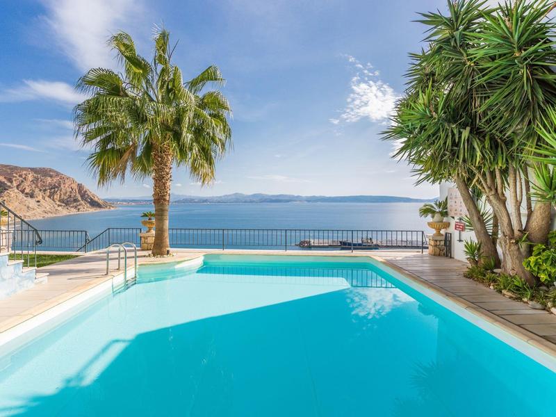 Zwembad met uitzicht op zee, palmbomen en zonneschijn.