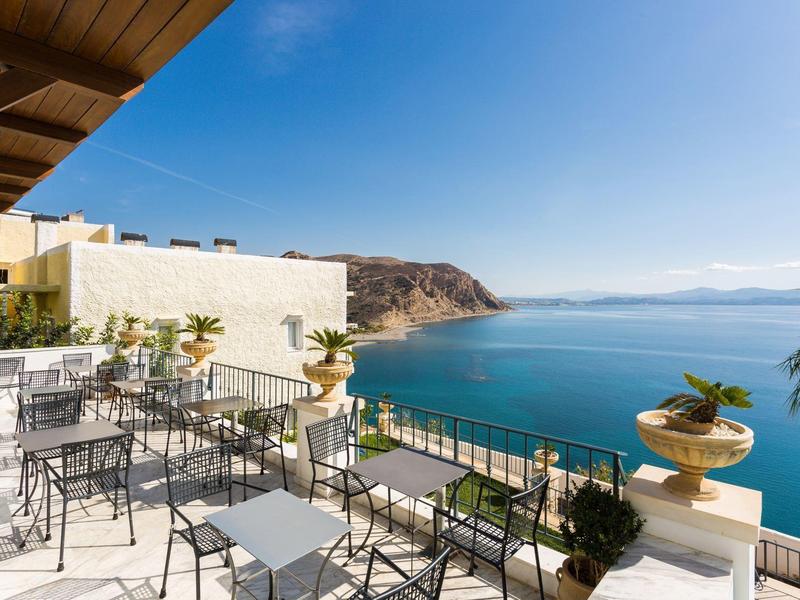 Terras met tafels en stoelen met uitzicht op zee en bergen.