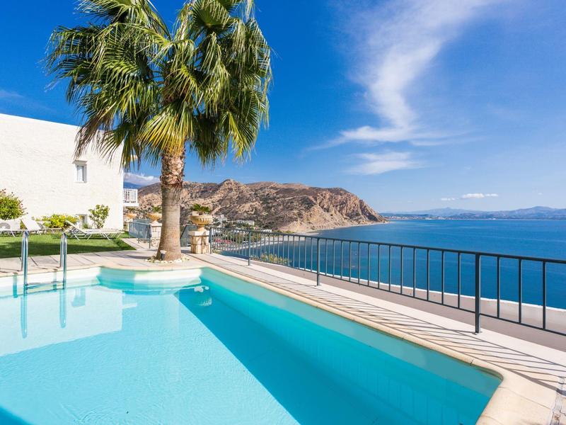 Zwembadterras met uitzicht op zee en palmbomen bij helder weer.