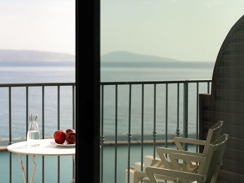 Uitzicht vanaf balkon met stoelen en tafel op rustige zee en verre eilanden.